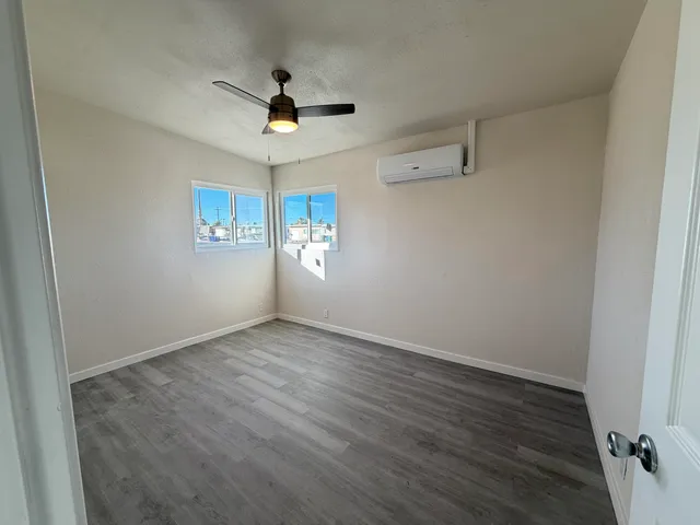an empty room with wooden floor chandelier fan and windows