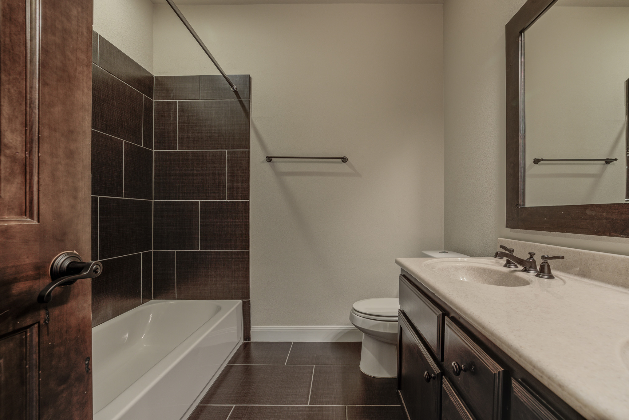4524 Berkman Drive Austin, TX 78723 - Photo 29 of 38 Full bathroom featuring wood-finish tile flooring, a tub-shower combination with dark large-format tile surround, a dark wood-finish vanity with dual integrated sinks, and bronze-finish fixtures