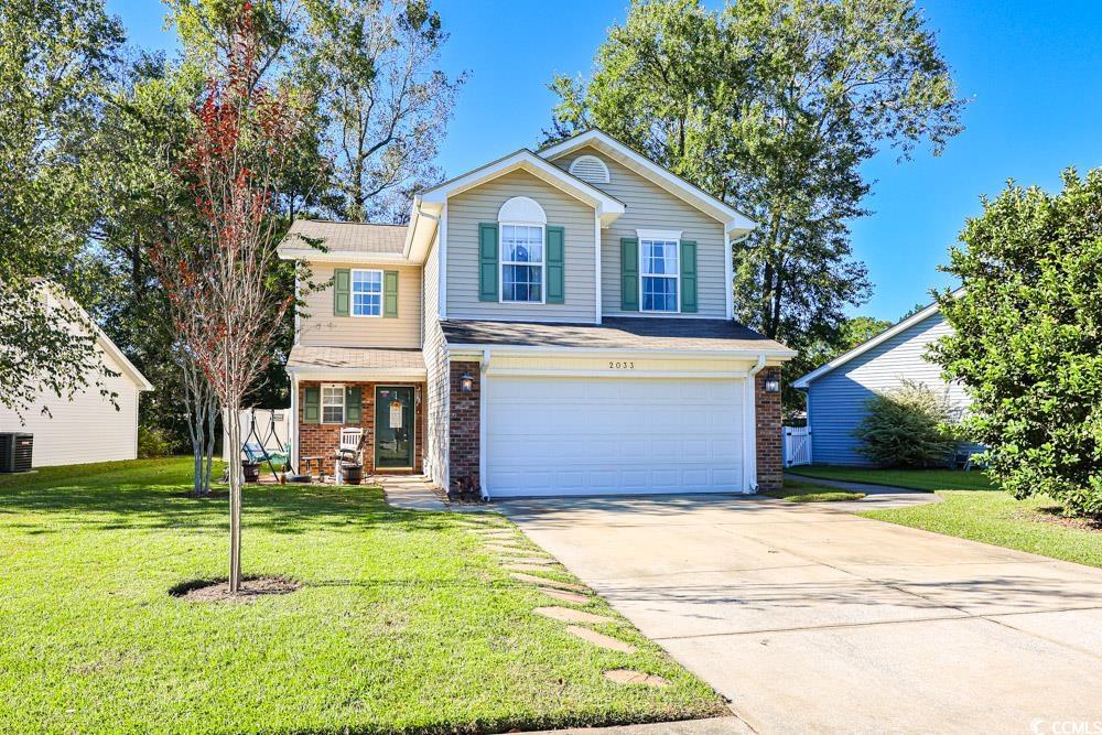 Traditional home featuring a garage, brick siding, concrete driveway, and a front lawn