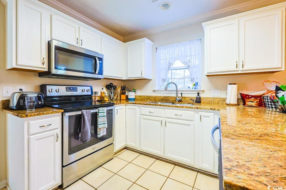 2033 Chadbury Lane Myrtle Beach, SC 29588 - Photo 6 of 39 Kitchen with appliances with stainless steel finishes, white cabinets, light tile patterned floors, light stone countertops, and crown molding