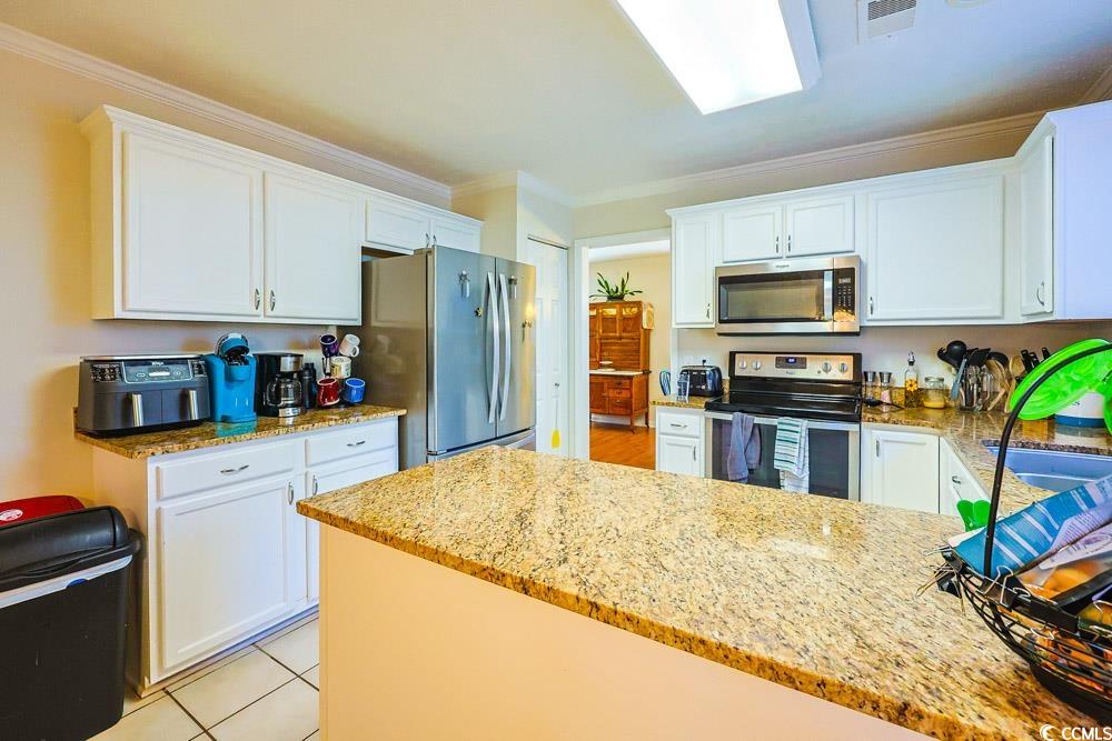 2033 Chadbury Lane Myrtle Beach, SC 29588 - Photo 7 of 39 Kitchen featuring appliances with stainless steel finishes, white cabinets, crown molding, light stone countertops, and light tile patterned floors