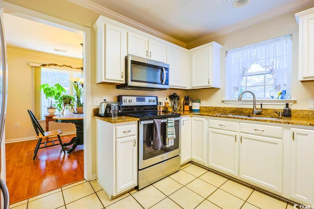 2033 Chadbury Lane Myrtle Beach, SC 29588 - Photo 10 of 39 Kitchen featuring stainless steel appliances, crown molding, white cabinetry, light tile patterned floors, and dark stone counters