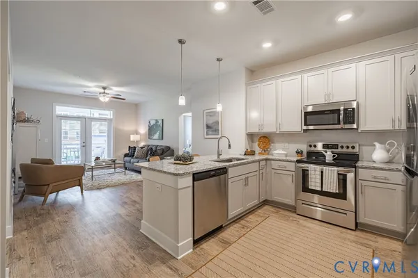 a kitchen with stainless steel appliances granite countertop a stove top oven a sink dishwasher a dining table and chairs with wooden floor