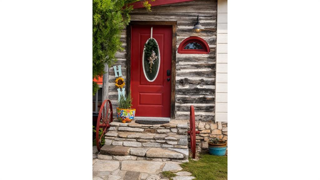Red entry door with oval glass insert, flanked by log siding and a stone foundation