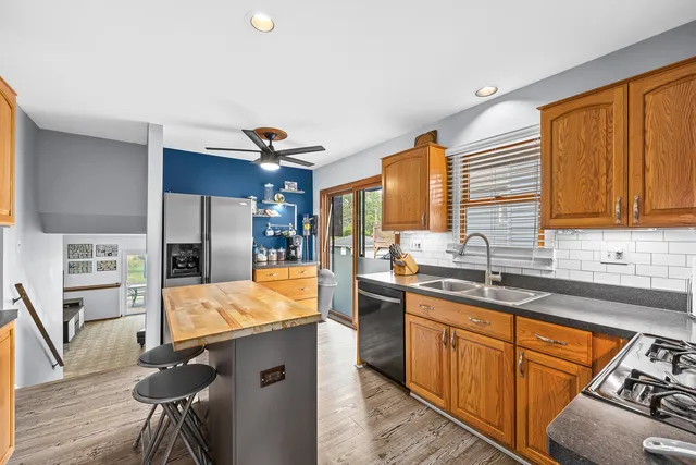 a kitchen with stainless steel appliances granite countertop wooden cabinets a sink dishwasher a stove and a refrigerator with wooden floor