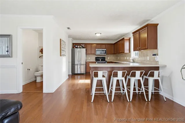 a kitchen with stainless steel appliances granite countertop a stove top oven a sink a dining table and chairs with wooden floor