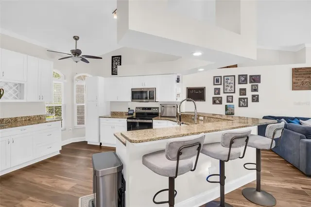 a kitchen with stainless steel appliances kitchen island granite countertop a stove top oven a sink a dining table and chairs with wooden floor