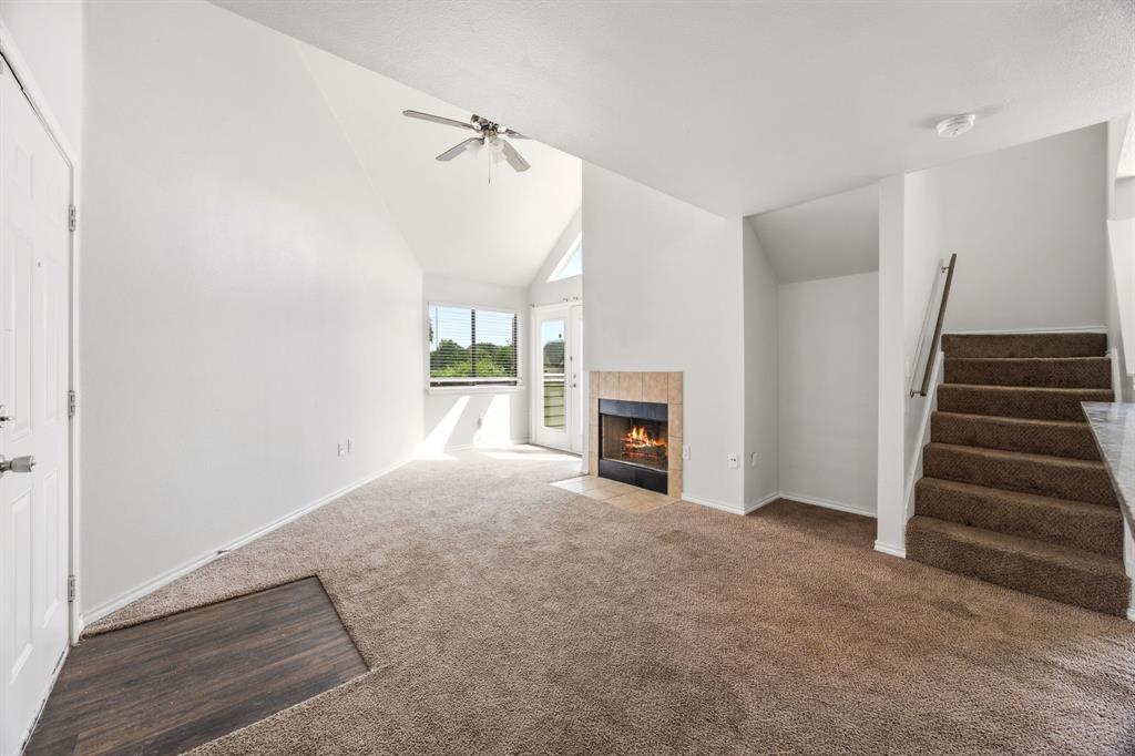9837 Walnut Street, Unit S203 Dallas, TX 75243 - Photo 2 of 26 Living area featuring vaulted ceilings, a ceiling fan, plush carpet, a fireplace with a tiled surround, and a staircase with a metal handrail