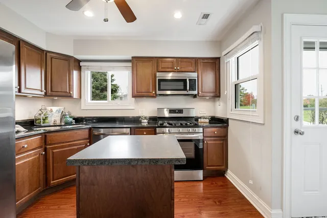 a kitchen with kitchen island granite countertop a stove top oven a sink dishwasher a refrigerator and a microwave oven with wooden floor