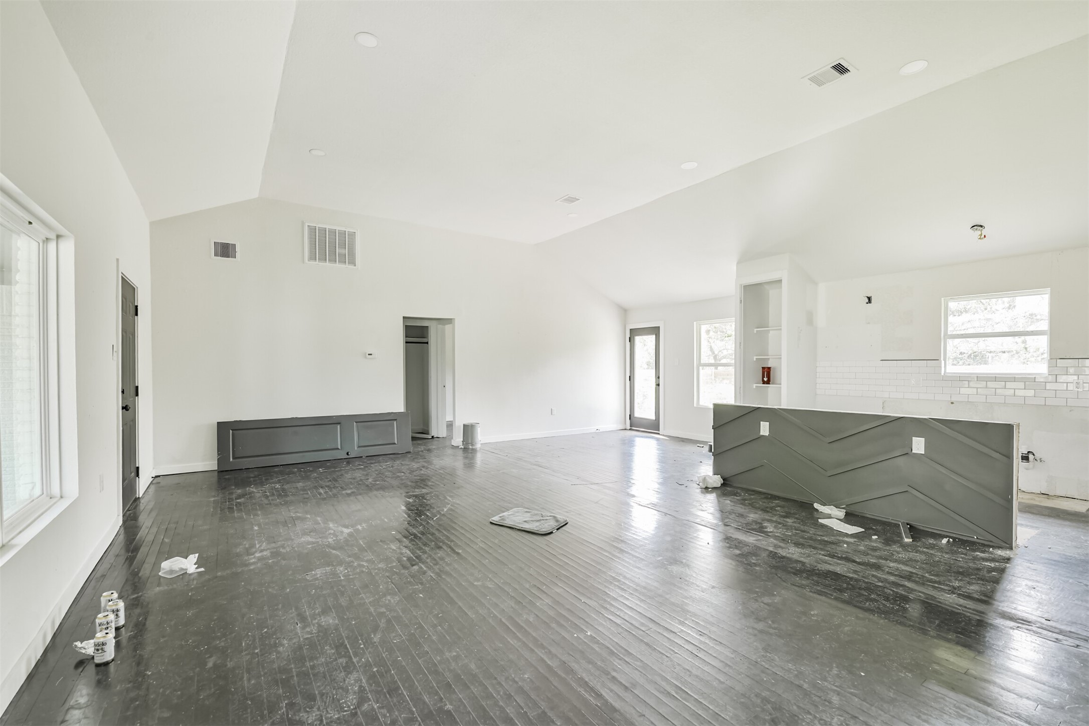 209 Leago Street Houston, TX 77022 - Photo 6 of 24 This spacious, open-concept room features high ceilings and abundant natural light from large windows. It has dark hardwood floors and a partially finished kitchen area with white subway tiles. Ideal for personalization and modern living.
