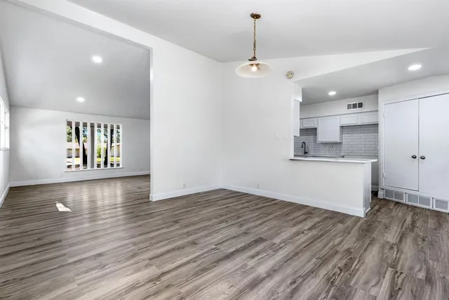 an empty room with wooden floor and kitchen view