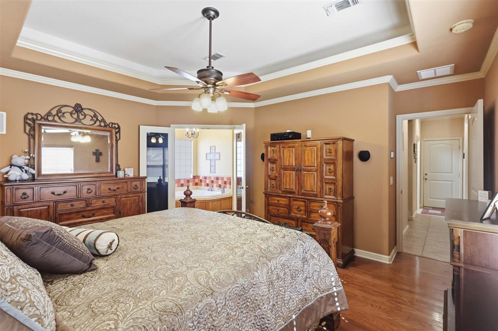 207 Dennis Road Lipan, TX 76462 - Photo 19 of 40 Recessed tray ceiling with crown molding, wood-finish flooring, ceiling fan with integrated lighting, and an alcove with a built-in jetted tub