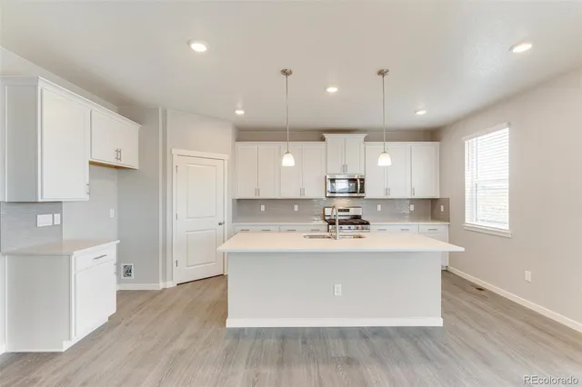 a view of a kitchen with kitchen island a sink wooden floor and stainless steel appliances