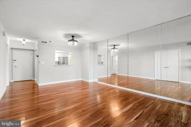 a view of an empty room with wooden floor and a kitchen