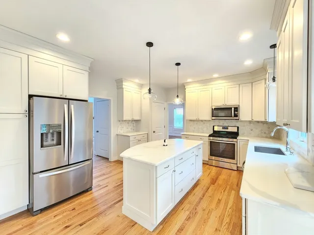 a large kitchen with stainless steel appliances a refrigerator a sink dishwasher a oven and a dining table with wooden floor