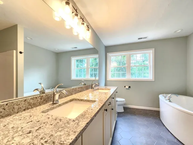 a bathroom with a granite countertop sink mirror bathtub and next to a window