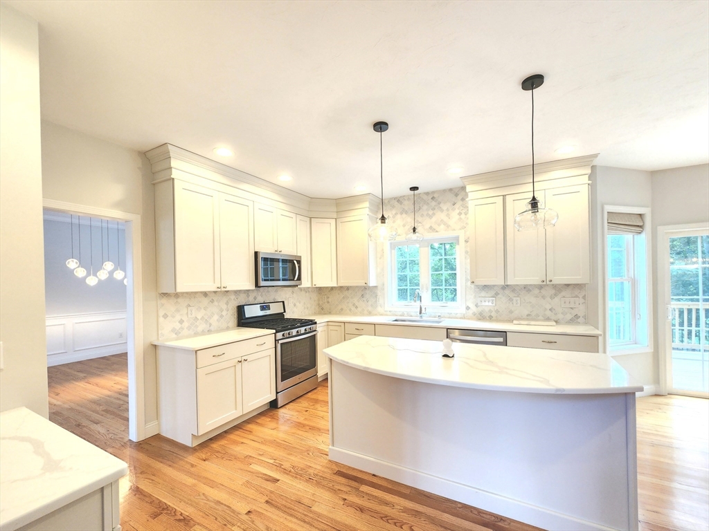 16 Exeter Road Hudson, MA 01749 - Photo 10 of 42 a large kitchen with kitchen island a sink a stove a refrigerator and white cabinets with wooden floor