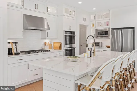 a kitchen with stainless steel appliances granite countertop a stove a sink a refrigerator and white cabinets with wooden floor