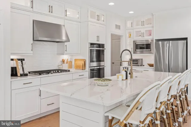 a kitchen with stainless steel appliances granite countertop a stove a sink a refrigerator and white cabinets with wooden floor