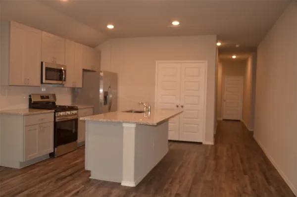 a kitchen with stainless steel appliances a stove top oven a sink a refrigerator white cabinets and wooden floor