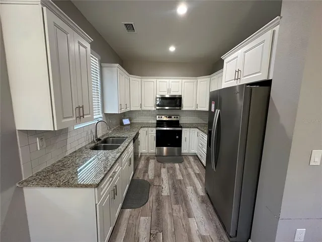 a kitchen with granite countertop a refrigerator a sink dishwasher a stove top oven a refrigerator and cabinets