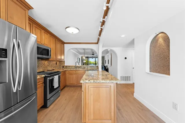 a kitchen with stainless steel appliances granite countertop a refrigerator a stove and a sink with wooden floor