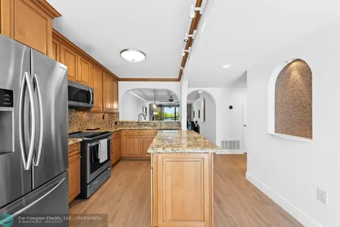 a kitchen with stainless steel appliances granite countertop a refrigerator a stove a sink a oven with white cabinets and wooden floor