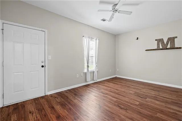 an empty room with wooden floor chandelier fan and windows