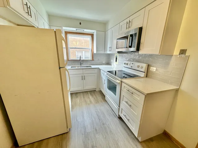 a kitchen with a sink a stove top oven a refrigerator a window and white cabinets