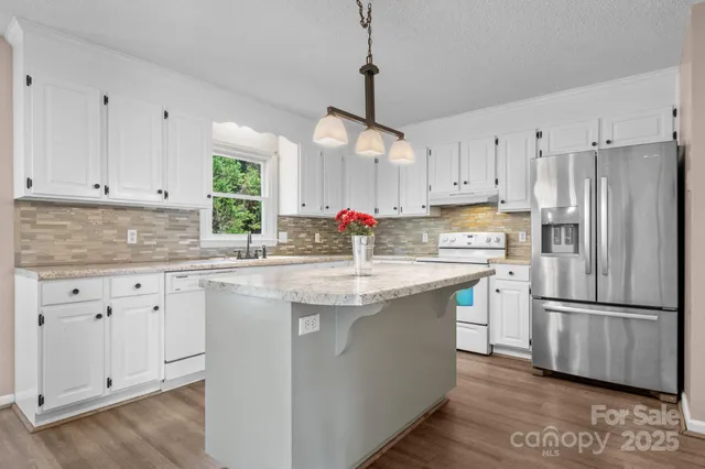 a kitchen with stainless steel appliances granite countertop a refrigerator a sink dishwasher a stove and white cabinets with wooden floor