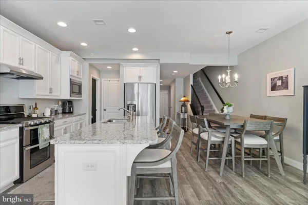 a kitchen with stainless steel appliances granite countertop a stove top oven a sink a dining table and chairs with wooden floor