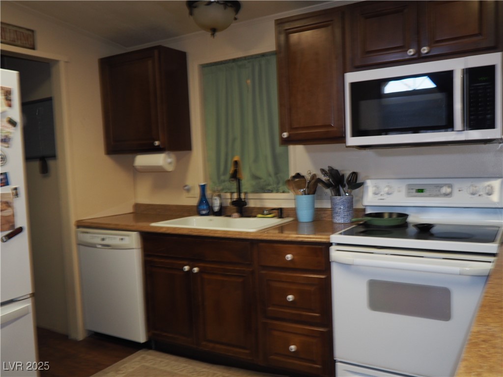3485 Gally Road Pahrump, NV 89060 - Photo 15 of 90 Kitchen with white appliances, ornamental molding, dark brown cabinets, light countertops, and wood finished floors