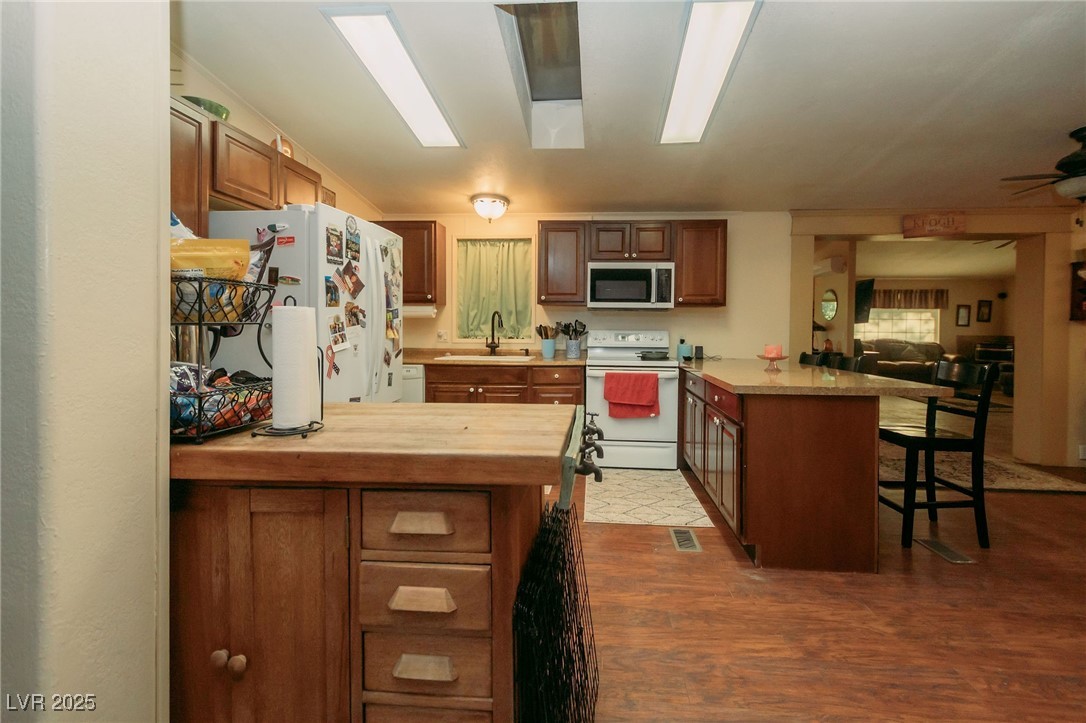 3485 Gally Road Pahrump, NV 89060 - Photo 90 of 90 Kitchen featuring a peninsula, white appliances, a kitchen breakfast bar, wood finished floors, and open floor plan