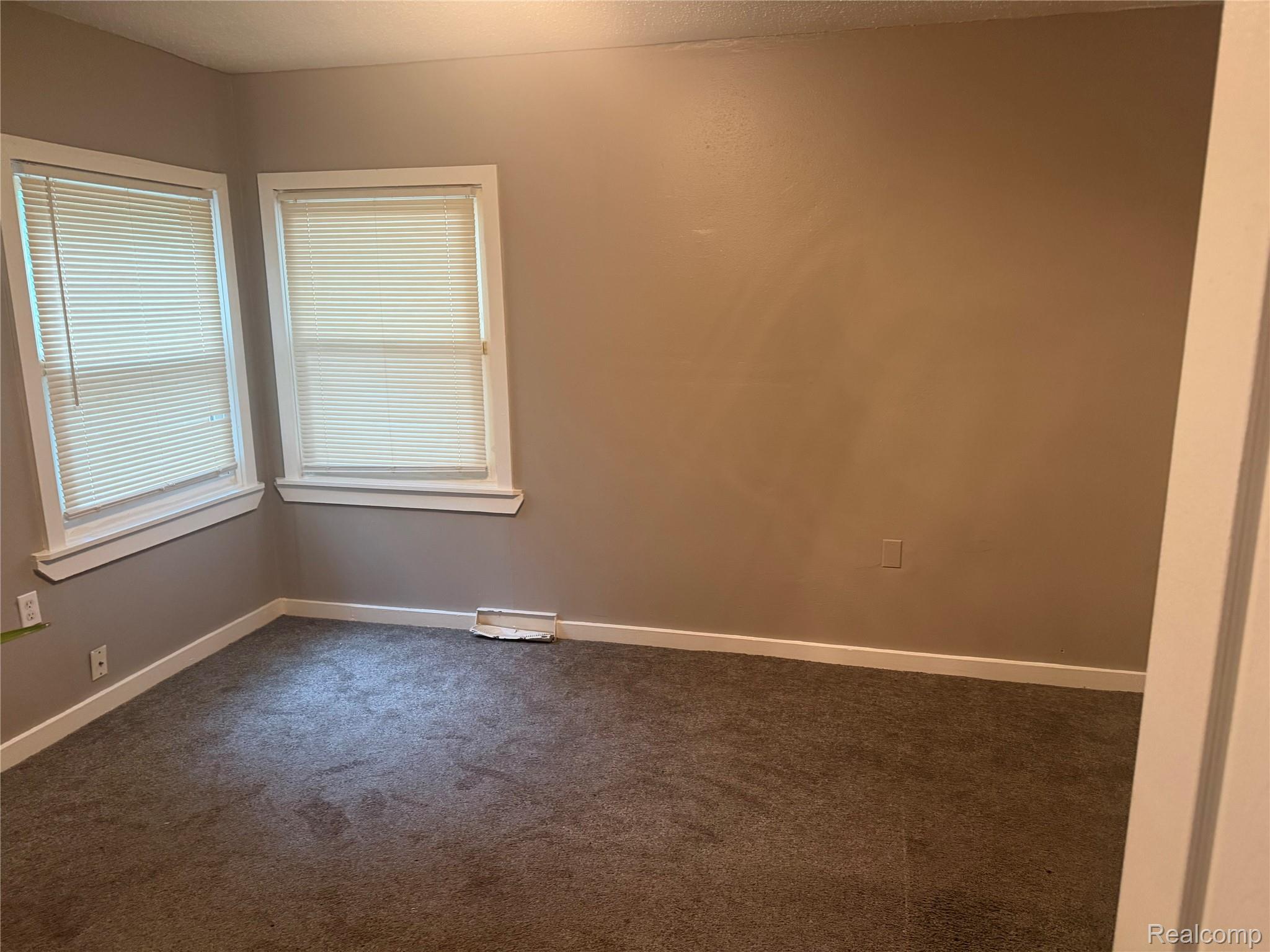 3322 Isabelle Street Inkster, MI 48141 - Photo 6 of 13 Carpeted room featuring two windows with white blinds, neutral wall paint, white trim, and a baseboard vent
