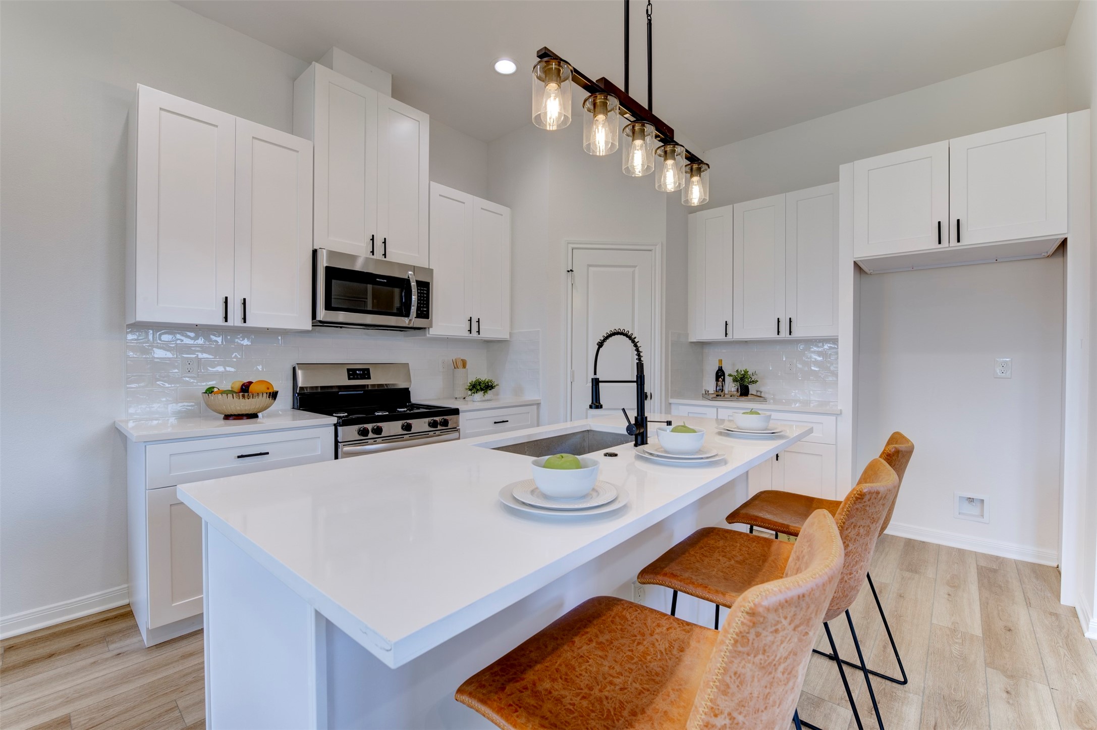 6807 Paris Street Houston, TX 77021 - Photo 23 of 50 Kitchen with white shaker cabinets, quartz countertops, subway tile backsplash, stainless gas range, stainless microwave, farmhouse sink on island, matte black coil-spring faucet, Edison rail pendant lighting, and leather bar stools. Pantry door visible at rear.