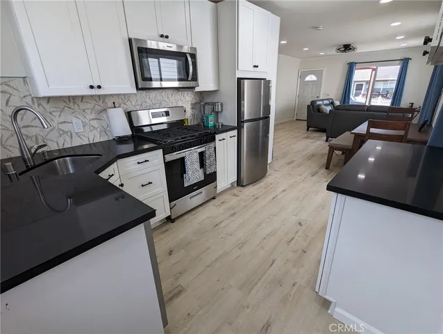 a kitchen with stainless steel appliances granite countertop a refrigerator a stove top oven a sink dishwasher and white cabinets