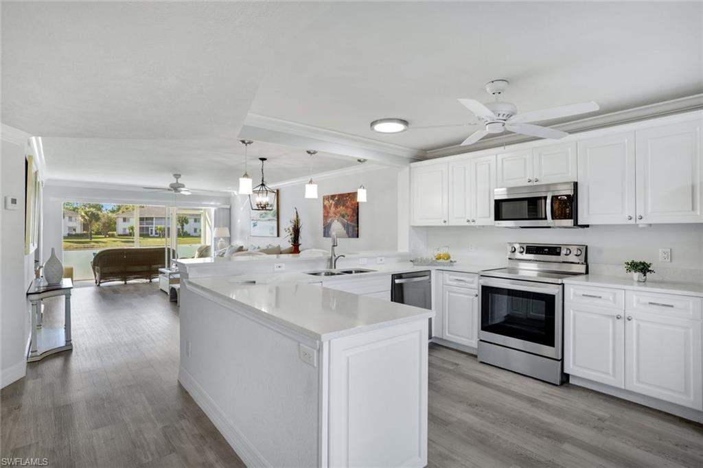409 Gabriel Circle, Unit 2203 Naples, FL 34104 - Photo 9 of 24 Kitchen featuring sink, kitchen peninsula, Coretex vinyl floors, white cabinetry, and stainless steel appliances