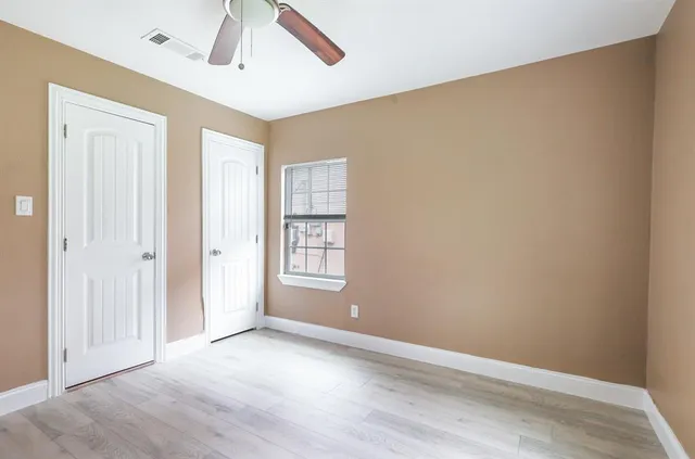 an empty room with wooden floor chandelier fan and windows