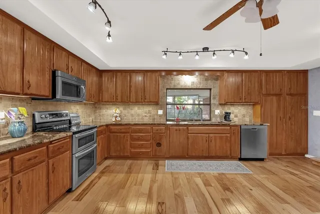 a kitchen with stainless steel appliances granite countertop wooden cabinets a stove top oven a sink and dishwasher with wooden floor