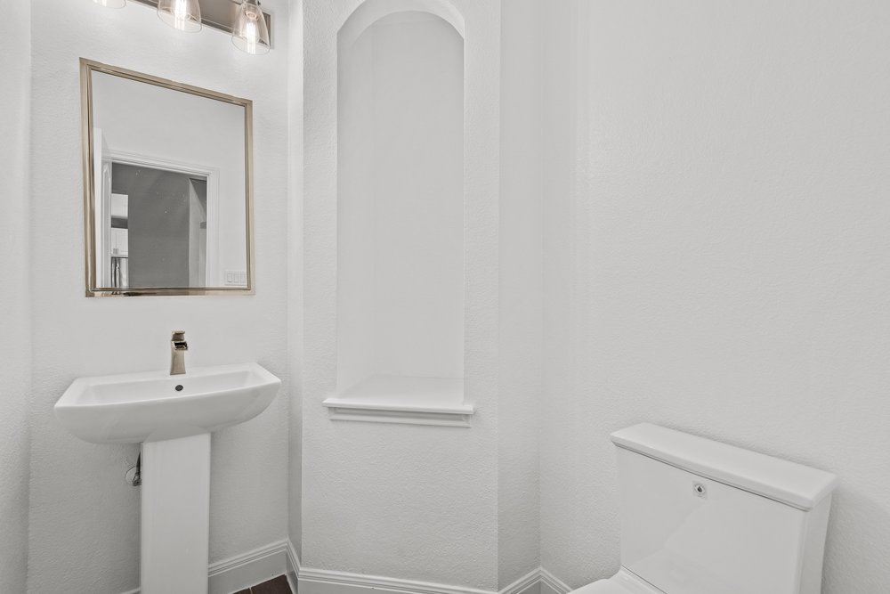 1815 Rue De St Tropez Austin, TX 78746 - Photo 22 of 40 White pedestal sink with a brushed nickel faucet, framed mirror, and a three-light vanity fixture