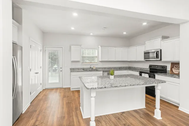 a kitchen with stainless steel appliances granite countertop a refrigerator a sink dishwasher a stove top oven a dining table and chairs with wooden floor