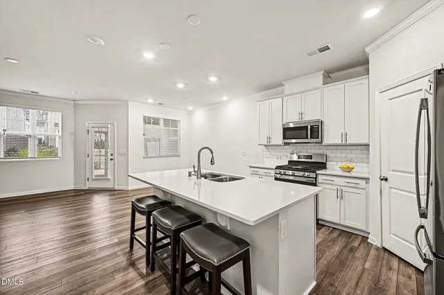 a kitchen with stainless steel appliances a stove a sink a refrigerator white cabinets and wooden floor