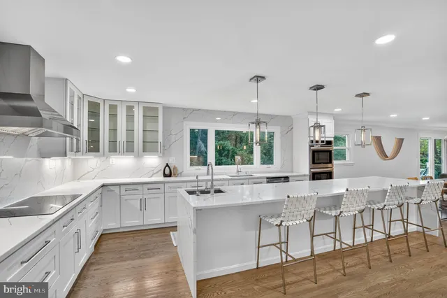 a kitchen with stainless steel appliances granite countertop a refrigerator a sink dishwasher a oven and a dining table with wooden floor