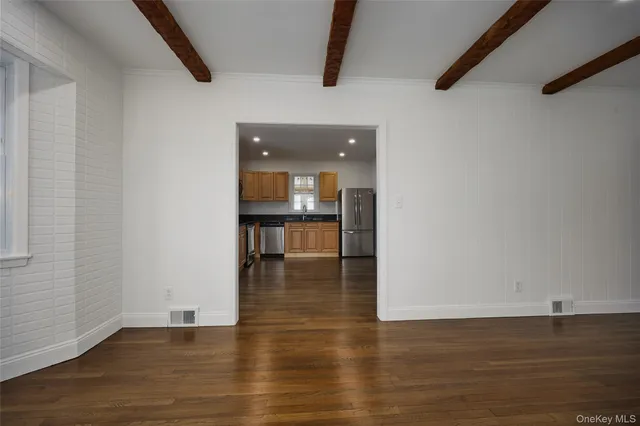 a view of empty room with wooden floor and kitchen view