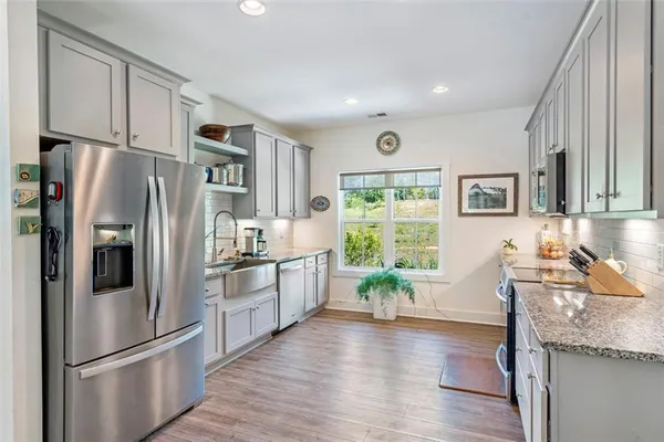 a kitchen with stainless steel appliances granite countertop a refrigerator a sink dishwasher a stove and white cabinets with wooden floor