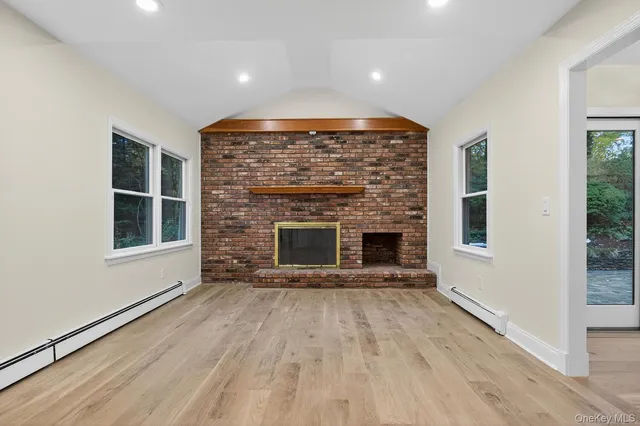 a view of an empty room with wooden floor fireplace and a window