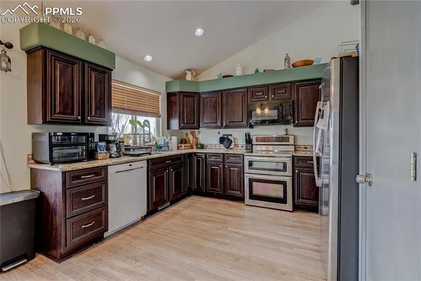 a kitchen with stainless steel appliances granite countertop a stove top oven a sink dishwasher and a refrigerator with wooden cabinets