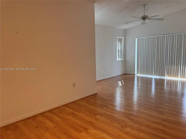an empty room with wooden floor ceiling fan and windows