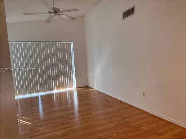 an empty room with wooden floor fan and windows