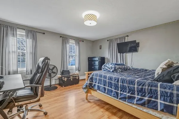 a bedroom with a bed a computer on the desk and a dresser next to a window